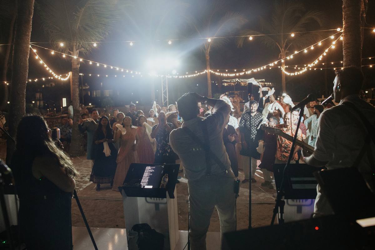 Live band performing at a beachside evening wedding reception under string lights
